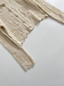 Détail du cardigan en maille crochetée crème avec motifs ondulés et boutons blancs
