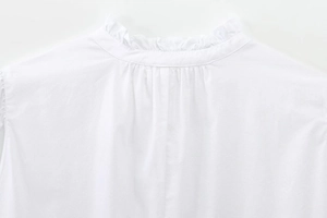 Detail of white cotton top featuring a ruffle stand collar and pleated back design