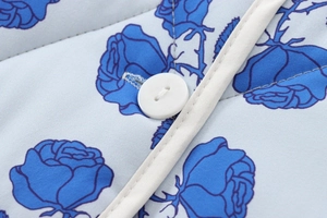 Detail of white button and blue rose print on smooth cotton fabric with piping