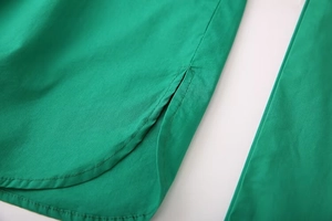 Detailed close-up of emerald green cotton linen shirt hem with fine stitching and side slit