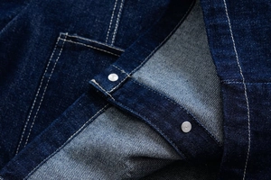 Detail of dark blue denim fabric with white contrast stitching and silver metal buttons
