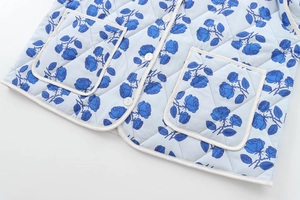 Detail of light blue quilted jacket featuring dark blue rose prints and white buttons