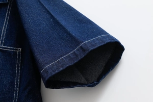 Detail of dark blue denim jacket featuring contrast white stitching and twill texture