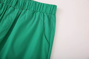 Detail of emerald green elastic waistband and side pocket stitching on women's trousers
