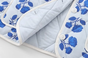 Close-up of diamond-quilted jacket featuring blue rose prints and white piping details