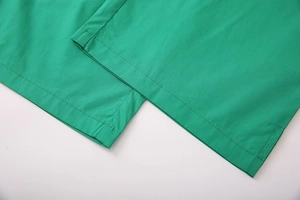 Detail of double-stitched hem on vibrant green woven trousers with precise seam work