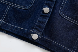 Detail of dark blue denim fabric featuring silver metal buttons and white contrast stitching