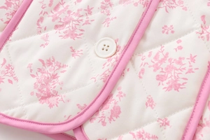 Close-up of floral quilted fabric featuring a white round button and pink piping details