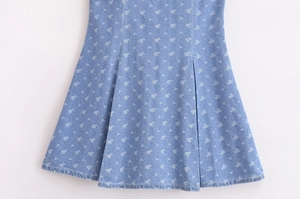 Detailed view of light blue denim dress featuring white floral print and pleated hem texture