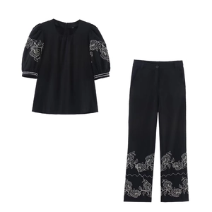 Detailed close-up of white floral embroidery on black puff sleeve top and trousers set