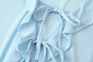 Detailed close-up of light blue fabric texture with ruffle trim and tie-front bow design