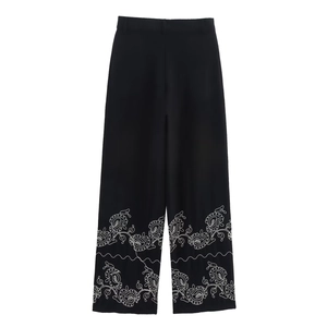 Detailed view of floral embroidery on the hem of high-waist black wide-leg trousers