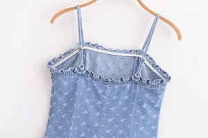 Detail of light blue denim dress with thin straps and ruffled neckline and floral print