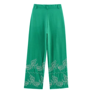 Close-up of emerald green wide-leg trousers featuring white floral embroidery at the hem