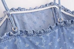 Detail of light blue denim top featuring floral print, ruffle neckline and adjustable straps