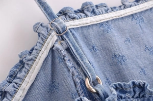 Detail of light blue denim dress with adjustable strap, silver buckle, and ruffle neckline