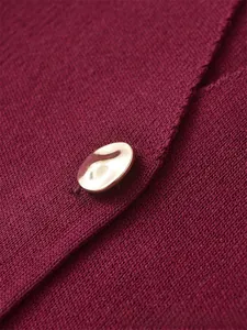 Macro shot of dark red knit fabric texture with an elegant irregular gold metal button