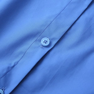 Close-up of bright blue fabric texture and matching four-hole button on the shirt