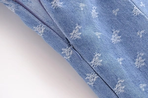 Detail of invisible zipper and white star embroidery on blue denim sundress fabric