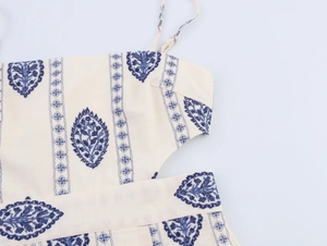 Detail of off-white dress featuring blue ethnic embroidery and side cutout design
