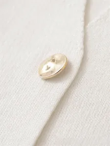 Close-up of a golden textured metal button on white knitted fabric for an elegant finish