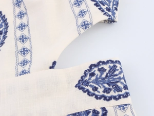 Macro detail of beige midi dress featuring blue embroidery and geometric cutout design