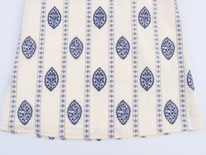 Detail of bohemian cream midi dress featuring blue embroidery and linen fabric texture