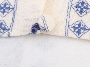 Detailed macro shot of beige cotton dress featuring blue geometric embroidery and fabric button