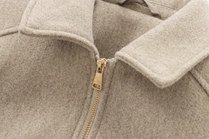 Detail of soft beige wool jacket showing gold zipper and lapel texture close-up