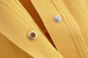 Vue détaillée de la texture du denim jaune avec des boutons-pression en métal argenté