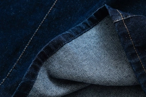 Close-up of dark blue denim fabric with twill texture and yellow contrast stitching