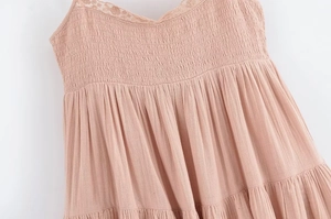 Détail d'une robe rose poudré avec dentelle, buste froncé et volants multicouches