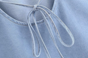 Detail of light blue denim top featuring an orange contrast stitching neckline and ties
