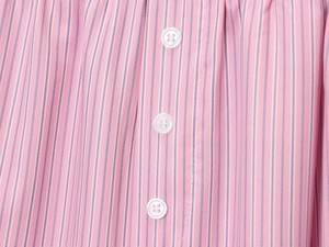 Dettaglio del tessuto a righe rosa e bianche con bottoni bianchi sulla pattina della camicia