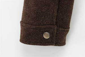 Detail of dark brown wool sleeve cuff with silver metal snap button on white background