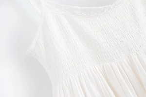 Détail d'une robe blanche à fines bretelles avec bustier smocké et coton texturé