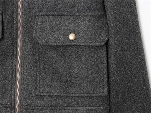 Detailed close-up of dark grey wool jacket featuring gold button and metal zipper detail