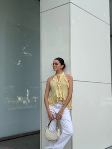Detail of a chic yellow halter neck ruffle top paired with classic white trousers