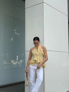 Detail of light yellow sleeveless halter top with layered ruffles and white trousers