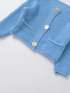 Detail of blue knit cardigan featuring golden metal buttons and textured pocket accents