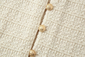 Détail du tissu en maille crème avec boutons dorés en relief sur un cardigan chic
