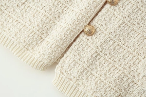 Detail von cremeweißem Grobstrick mit verzierten goldenen Wappenknöpfen für Luxus-Optik