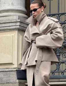 Detail of a khaki loose fit trench coat and split skirt in an outdoor urban setting