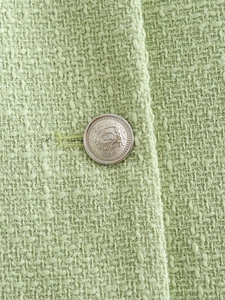 Detailed close-up of light green tweed fabric texture and silver embossed metal button