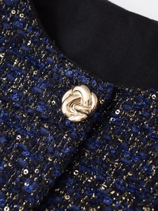 Detailansicht von blauem Tweed-Stoff mit Goldpailletten und einem Metall-Blumenknopf