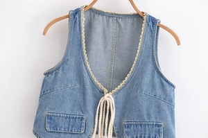 Détail d'un gilet en jean à col en V avec dentelle crème et laçage sur un cintre en bois