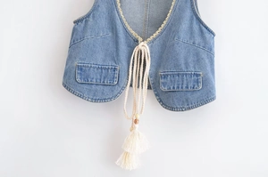 Détail d'un gilet en jean vintage avec bordure en dentelle blanche et cordons à pompons