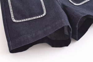 Detail of dark blue denim shorts featuring white contrast stitching on the front pocket