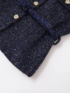 Detailaufnahme von dunkelblauem Tweedstoff mit Goldfäden und dekorativem Reliefknopf