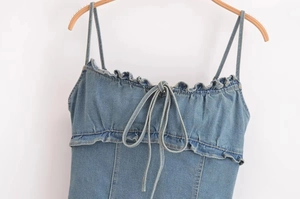 Dettaglio del top in denim azzurro con bordi a balze e design con lacci sul davanti